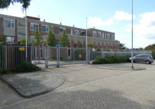 Schoolgebouw met een rij parkeerplaatsen gelegen aan het hek