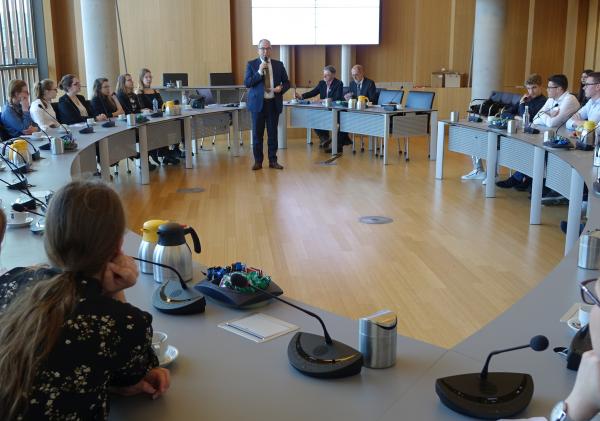 Raadszaal met wethouder André van der Reest. Leerlingen zitten aan de omringende tafels