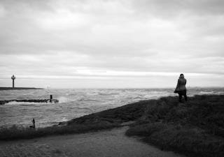 Zwart-wit foto van storm Ciara, een vrouw staat op de duinen te kijken naar de zee
