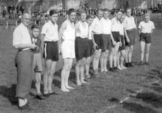Groepje jongens staan op een rij in een sporttenue, links vooraan de coach in nettere kleding