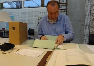 André van Noort zit aan een tafel met archiefstukken in de studiezaal