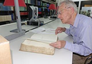 Dirk Kolff bladert door oud boek aan tafel in de studiezaal