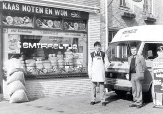 Winkel met reclamebord "kaas noten en wijn". 2 mannen staan buiten de zaak bij een busje