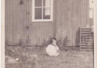 Baby zit op het gras voor een barak