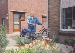 Vrouw staat met haar fiets in de voortuin van haar huis