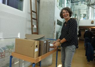 Thea van Dijk in de studiezaal, ze staat naast een kar met archiefdozen