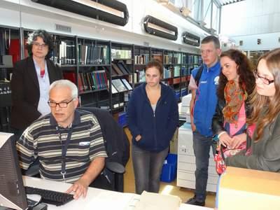 Archiefmedewerker Martin Zuidhof laat de leerlingen en docente (tweede van rechts) zien hoe je oude kaarten van Goes in een database opzoekt