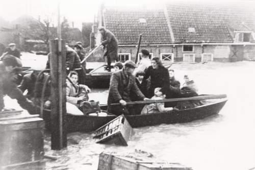 Foto van een overstroomd gebied met mensen die in een bootje vervoerd worden