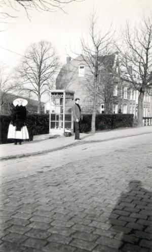 Een man staat buiten bij een telefooncel en een vrouw in Zuid-Bevelandse strekdracht staat twee meter verderop