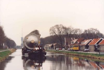Een grote tank wordt verveord over het kanaal met aangelegen huizen en geparkeerde auto's rechts