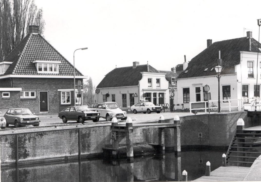 De haven, een paar auto's staan geparkeerd aan het weten en er zijn 3 huizen te zien op de foto