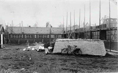 Een school wordt gebouwd, materialen staan op een veldje naast het bouwwerk.