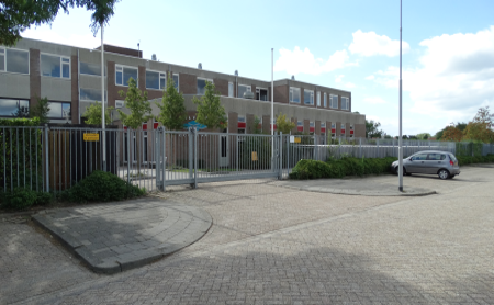 Schoolgebouw met een rij parkeerplaatsen gelegen aan het hek