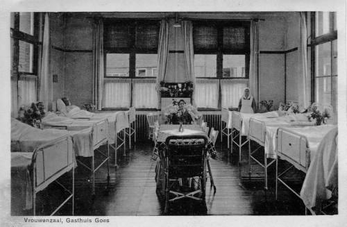 Vrouwenzaal in het ziekenhuis. Aan beide kanten van de ruimte zijn vier bedden te zien, en één staat tegen de achtermuur.