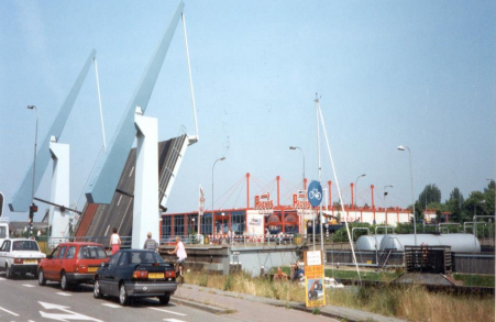 auto's staan te wachten tot de ringbrug naar beneden gaat. Op de achtergrond is het pand van de Praxis te zien