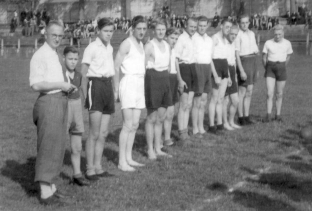 Groepje jongens staan op een rij in een sporttenue, links vooraan de coach in nettere kleding
