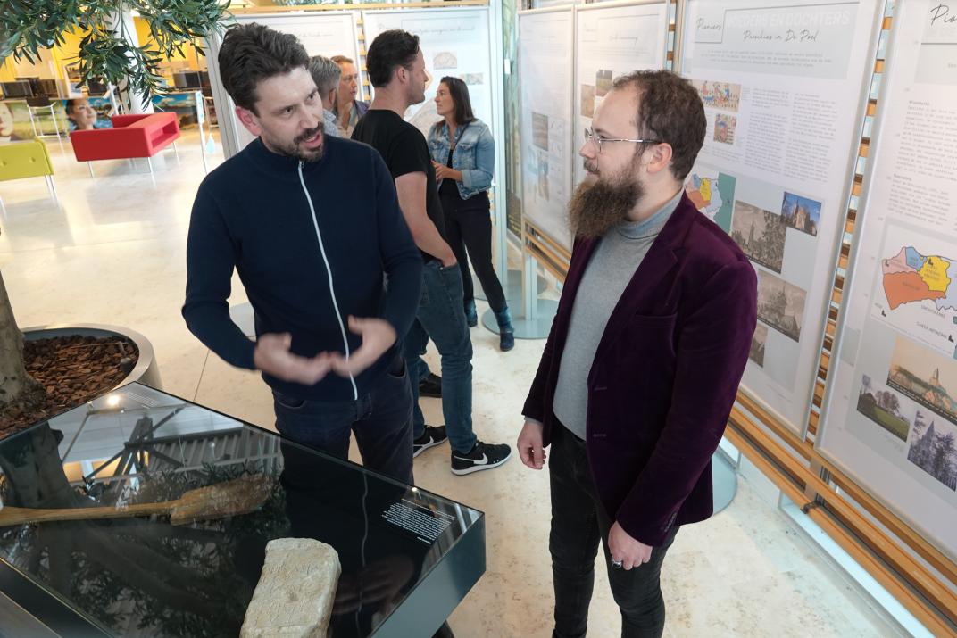 Archeoloog Karel-Jan Kerckhaert en wethouder Martijn Vermeulen tijdens de opening bij de vitrine met de votiefsteen. Achter hun staan bezoekers de panelen te bespreken.