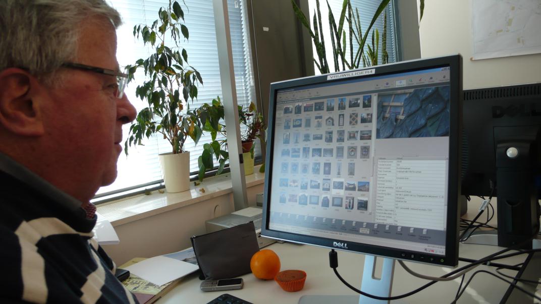 Rinus kijkt naar het beeldscherm van zijn computer, waarop pictogrammen van foto's te zien zijn