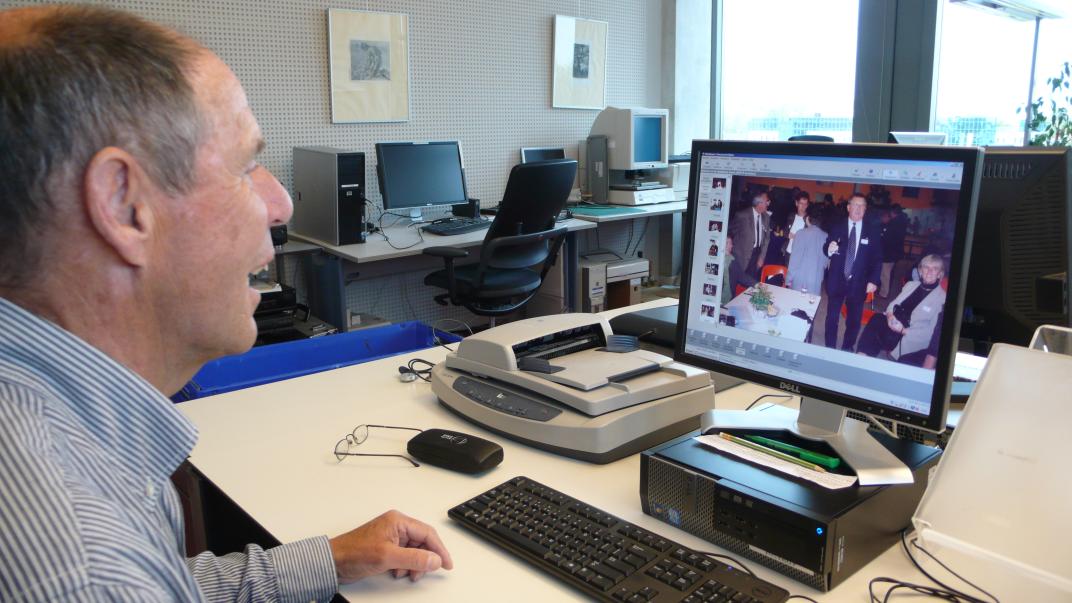 Adri Biersteker zit achter een computer, op het beeldscherm staat een foto met 4 mensen