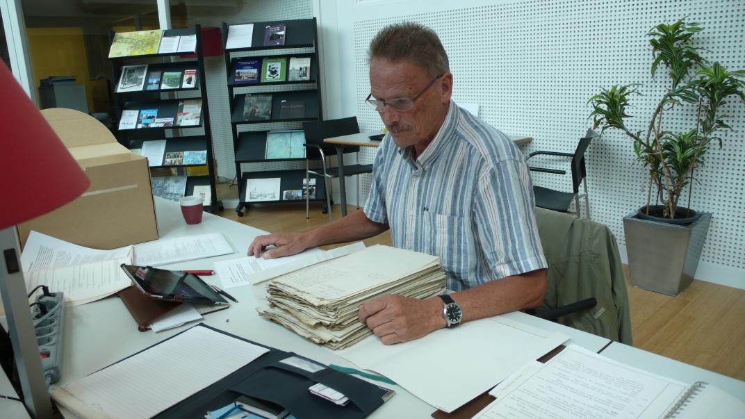 Frits de Kaart zit aan een tafel in de studiezaal met een stapel papier voor zich