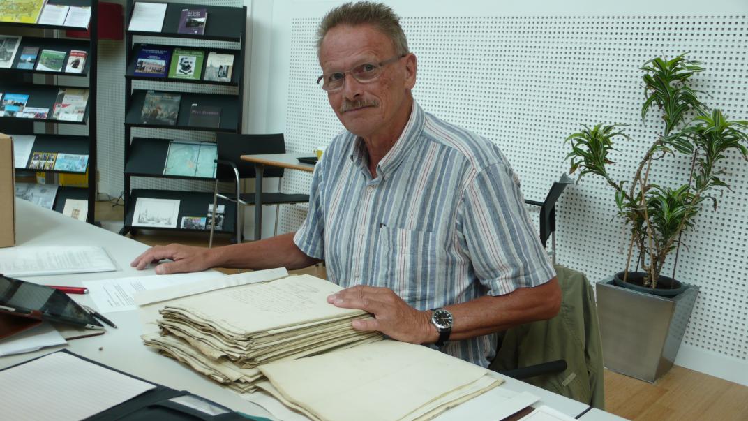Frits de Kaart zit aan een tafel in de studiezaal met een stapel papier voor zich