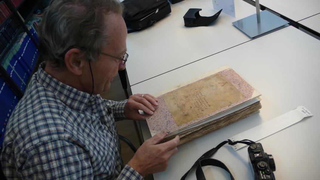Chiel Smallegange zit aan tafel en kijkt naar een ingebonden boek met akten