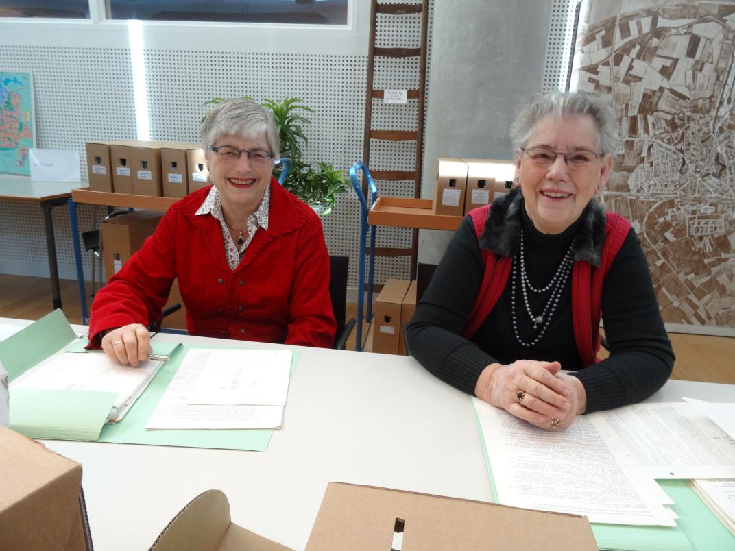 Joke Smallegange (links) en Lenie Wondergem aan een tafel vol archiefstukken in de studiezaal