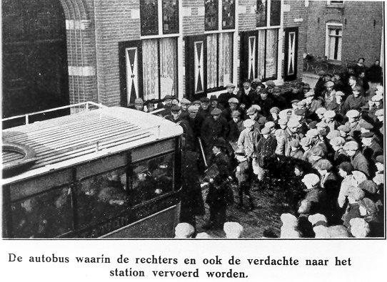 Een grote groep mensen staat buiten achter een bus. Eronder staat genoteerd "De autobus waarin de rechters en ook de verdachte naar het station vervoerd worden."