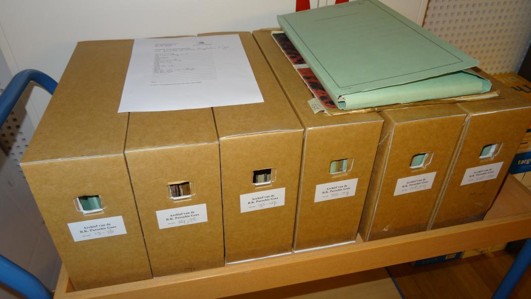 Archiefdozen op een kar, bovenop ligt een papier met het inventaris en wat losse stukken