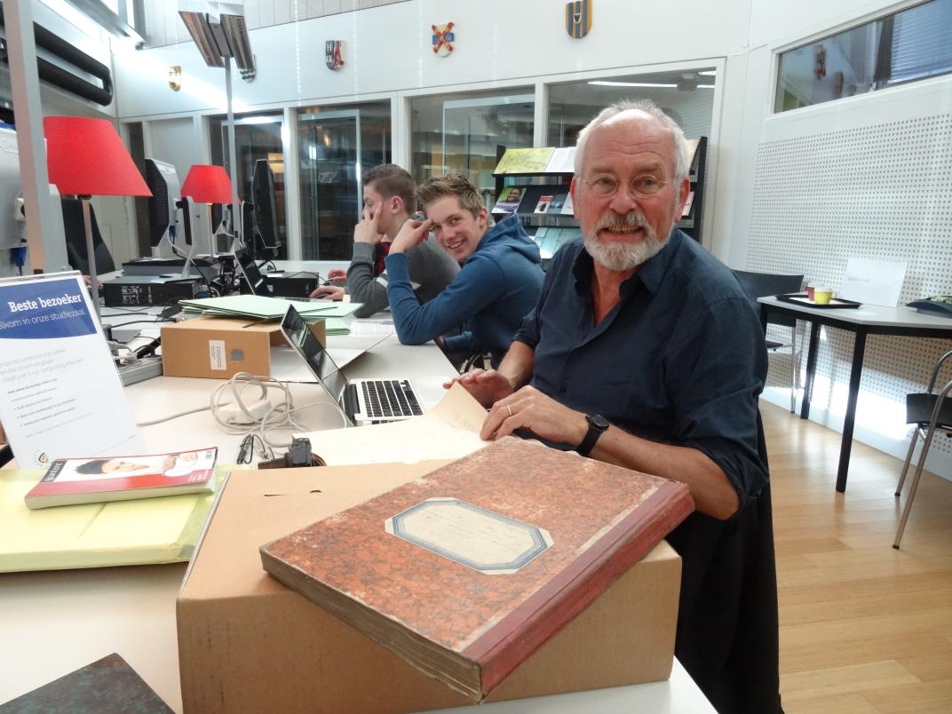 Dick van Halsema zit aan een tafel in de studiezaal met onderzoeksmateriaal voor zich
