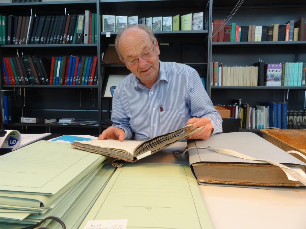 Han Vermeulen kijkt in een boek op de studiezaal. Op de tafel voor hem liggen nog nog meer stukken uit het archief