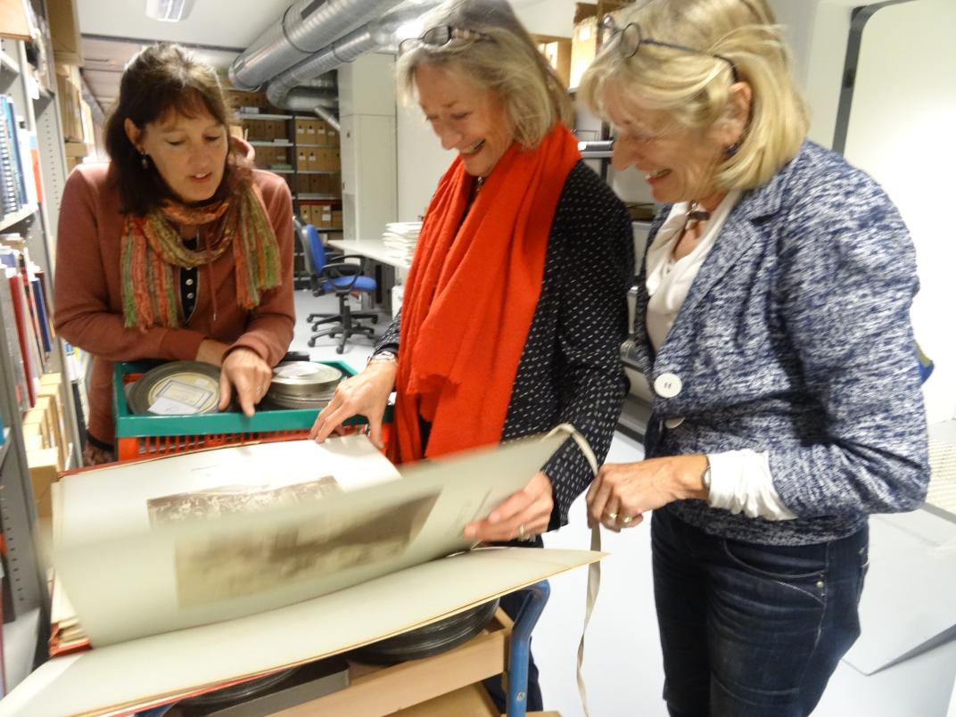 3 vrouwen bladeren door een groot boek met foto's 