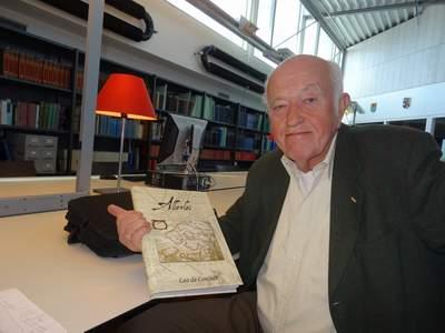 Leo de Coninck aan tafel in de studiezaal, hij presenteert zijn boek aan de camera