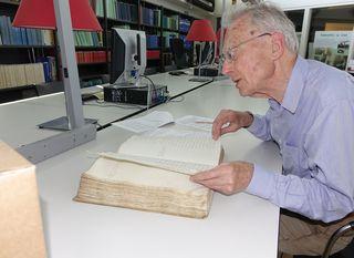 Dirk Kolff bladert door oud boek aan tafel in de studiezaal