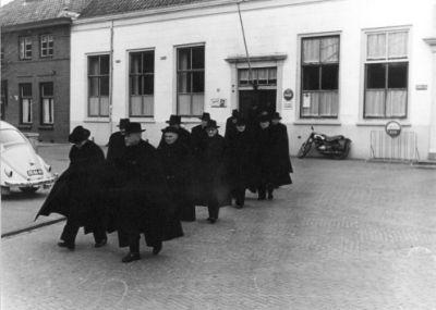 Rouwstoet van mannen die uit de herberg gelopen komt