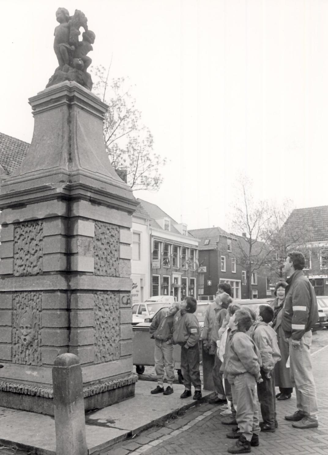 Stadswandeling met leerlingen van de Christelijke Basisschool De Welle op de Beestenmarkt. De kinderen staan rondom en kijken naast de fontein met hun leraar