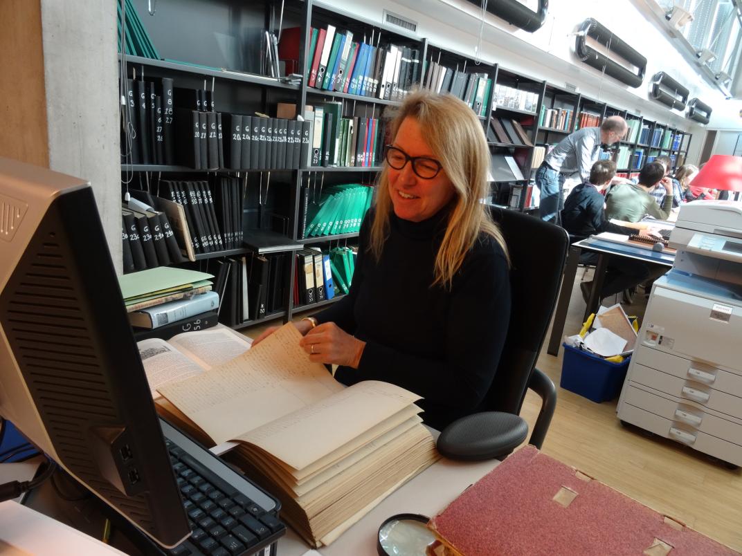 Sandra den Dulk achter een bureau vol archiefmateriaal