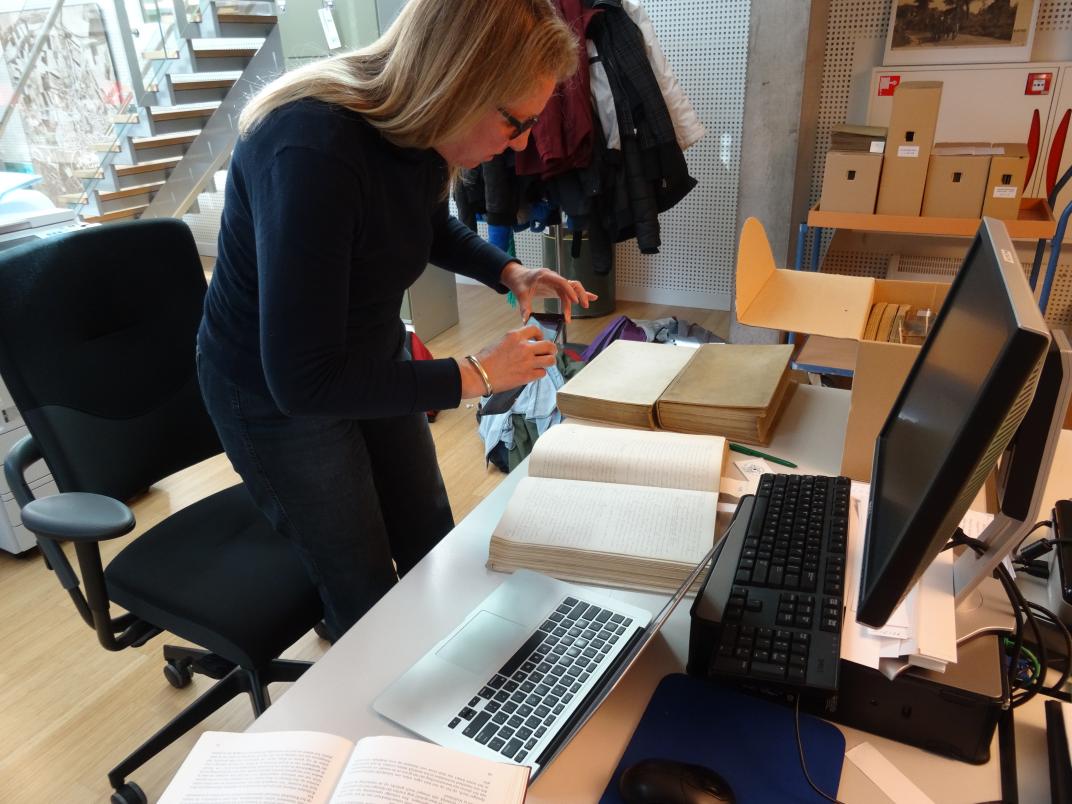 Sandra den Dulk achter een bureau vol archiefmateriaal