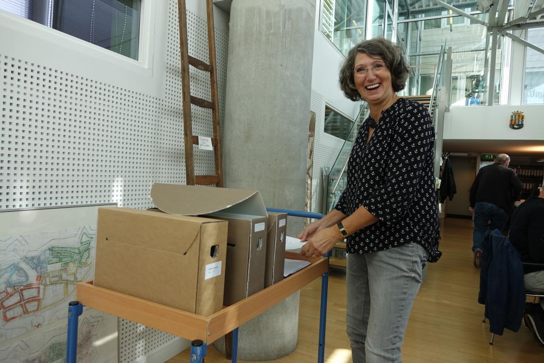 Thea van Dijk in de studiezaal, ze staat naast een kar met archiefdozen